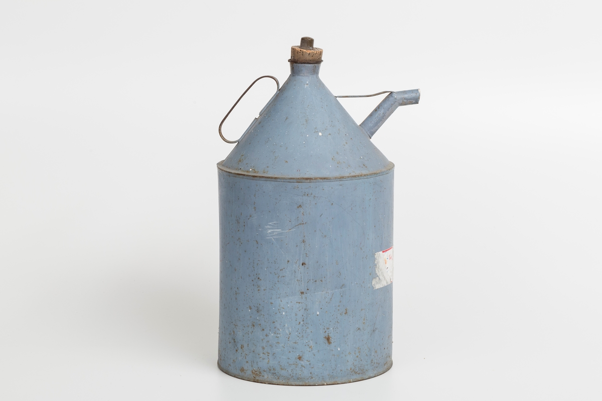 Kanne i sink, blå. Korket i tuten og korklokk med plast. Har håndtak og helletut. Kannen har påklistret god jul merkelapp med navn. Delvis avrevet.