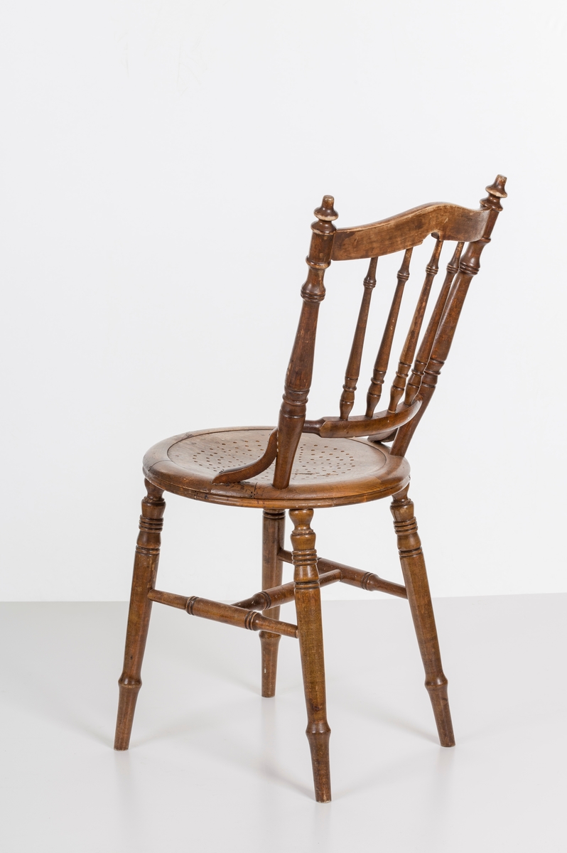 Stol i lakket treverk. Rundt stolsete med hullemønster. Rygg som er svakt buet med spiler og mønster. Dreide ben om spiler i rygg.