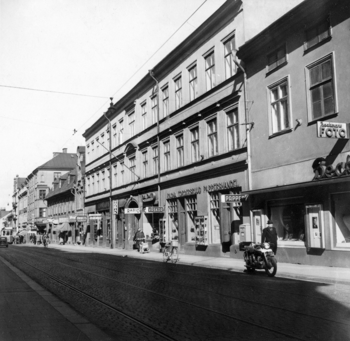 På femtiotalet, före 70- och 80-talens gatubreddning, var Kungsgatan en uttalad affärsgata och Ettans spårvagnslinje traffikerade fram till 1958 även denna del av staden. 
Kungsgatan var då uppdelad i norra och västra Kungsgatan med Bergsbron som avdelare.
På bilden ses en del affärsgatan med butiker som Beckmans Foto, Toblers Frukt och Choklad, Köhlers Mode, Norra Päls - Hatt- & Mössaffären, Granstrands broderiaffär, Weydes, med mera.
