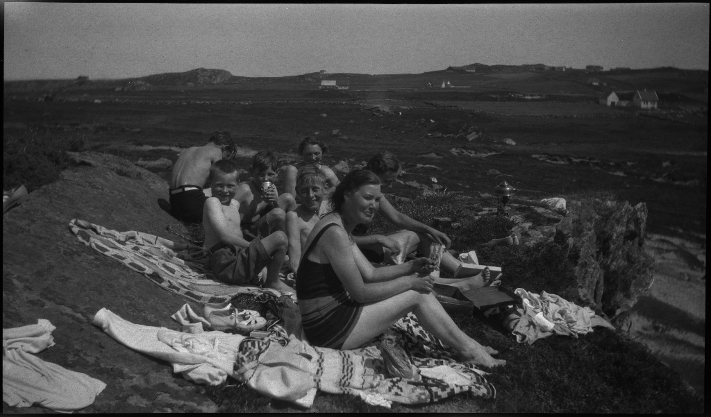 Barn og unge på og rundt stranda i Vigdelsvika. De fleste har satt opp telt, noen soler seg og noen bader. Den ene gutten på bilde nr. 6 holder et flytebelte.