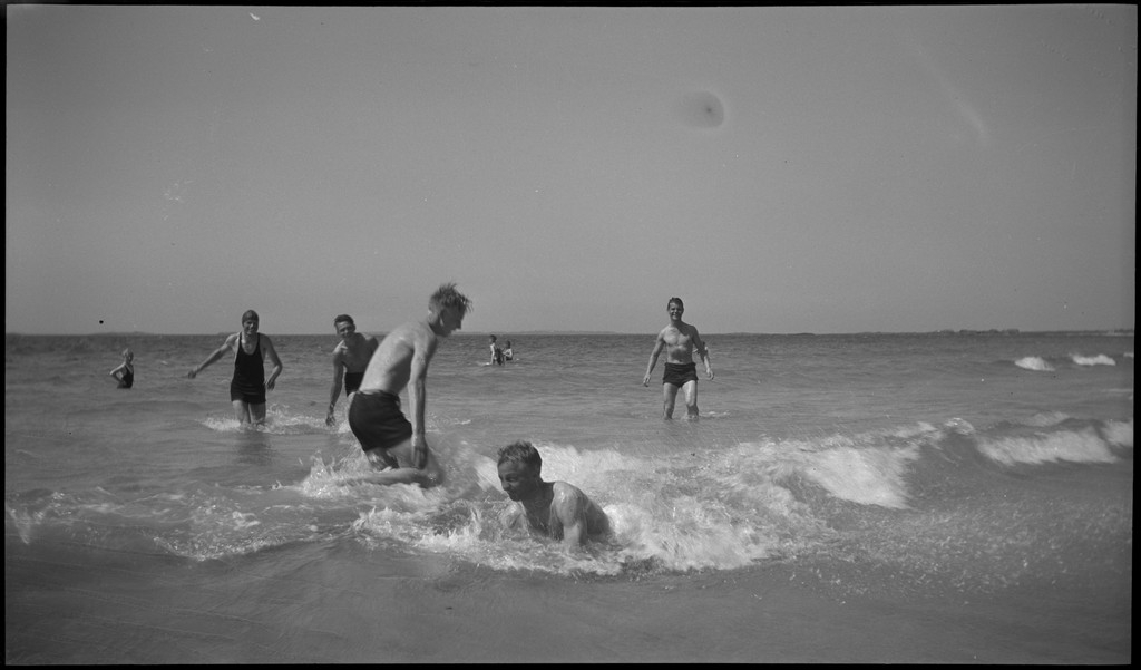 En stor vennegjeng i lystig lag på stranda på Sola. De har trommer og trekkspill og leker i vannet og på land med og uten ball. Sola strandhotell ligger i bakgrunnen. Tor Johannessen og Harald Bergsaker er på bilde nr. 14 og 18.
