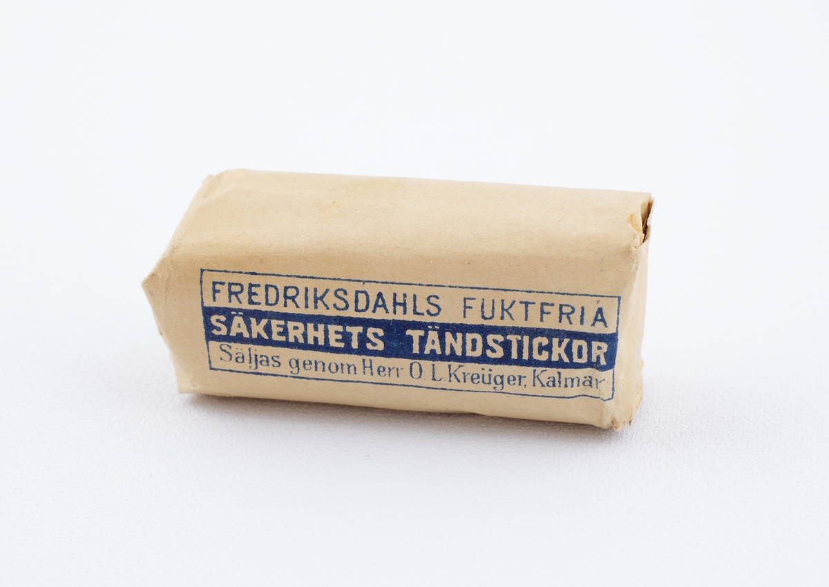 Tändsticksask.
Rektangulär modell. Blåvit text på omslutande etikett: "Fredriksdahls Fuktfria Säkerhets Tändstickor, Säljas genom Herr O.L. Kreüger, Kalmar".