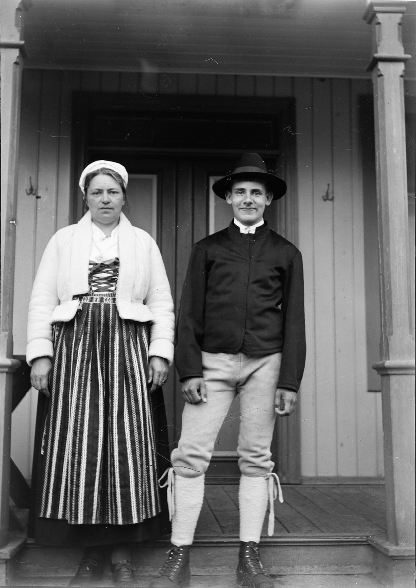 Christiane Liljefors med sonen Roland, klädda i Leksandsdräkter, står på trappan framför bostadshus, sannolikt på Svensgården, Dalarna, Sverige