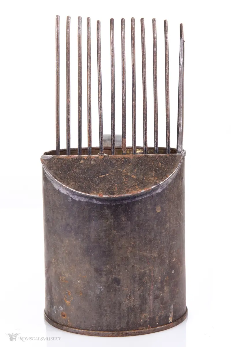 Sylinderformet blikkboks som kropp, med påloddet buehåndtak og en skråstilt plate med tenner foran.