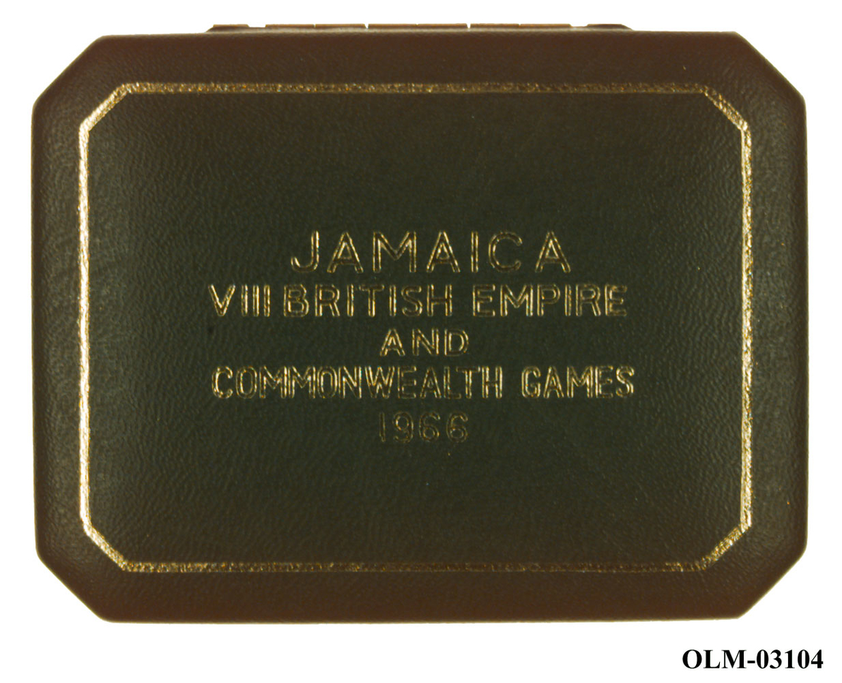 Sølvmynt med en kjede langs kanten, en krone øverst og tekst i midten. På baksiden en kvinne med fruktkurv og en mann med bue, mellom dem et våpenskjold med en krokodille øverst. Mynten ligger i en eske.