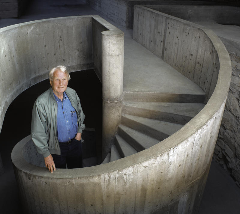 Arkitekt Scerre Fehn poserer i den spiralformede betongtrappa i Storhamarlåven. På seg har han en lys, åpen jakke og blå skjorte. Han holder høyre hånd på betongrekkverket.