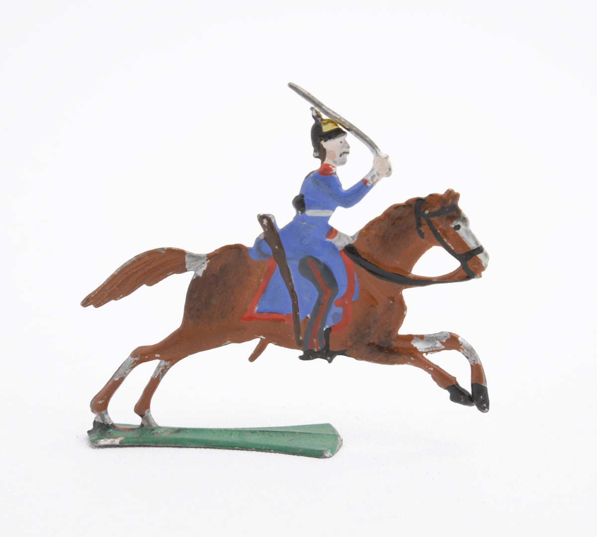 Ryttare till häst i blå uniform med dragen sabel. Han är även utrustad med koppel och pickelhuva. Sadeln är blå med röda kanter. Hästen brun på grön platta.
Inskrivet i huvudkatalog 1963.