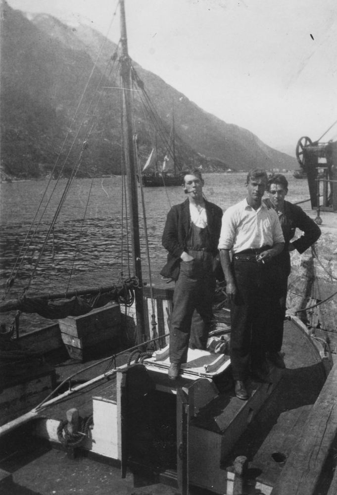 3 personer, kan være søsken fra Juvikøra, avbildet ombord i båt ved kaia til Jacobsenbrygga i Sjøgata (Trolig listerbåt).
Ute på elva ser vi ei Jakt eller Galeas?
