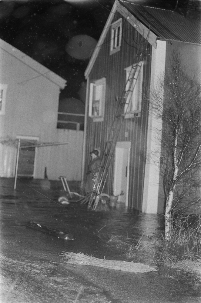 Flom i Mosjøen November 1971. 2 menn utenfor  Sjøgata 31, brygga har vann oppetter veggen.