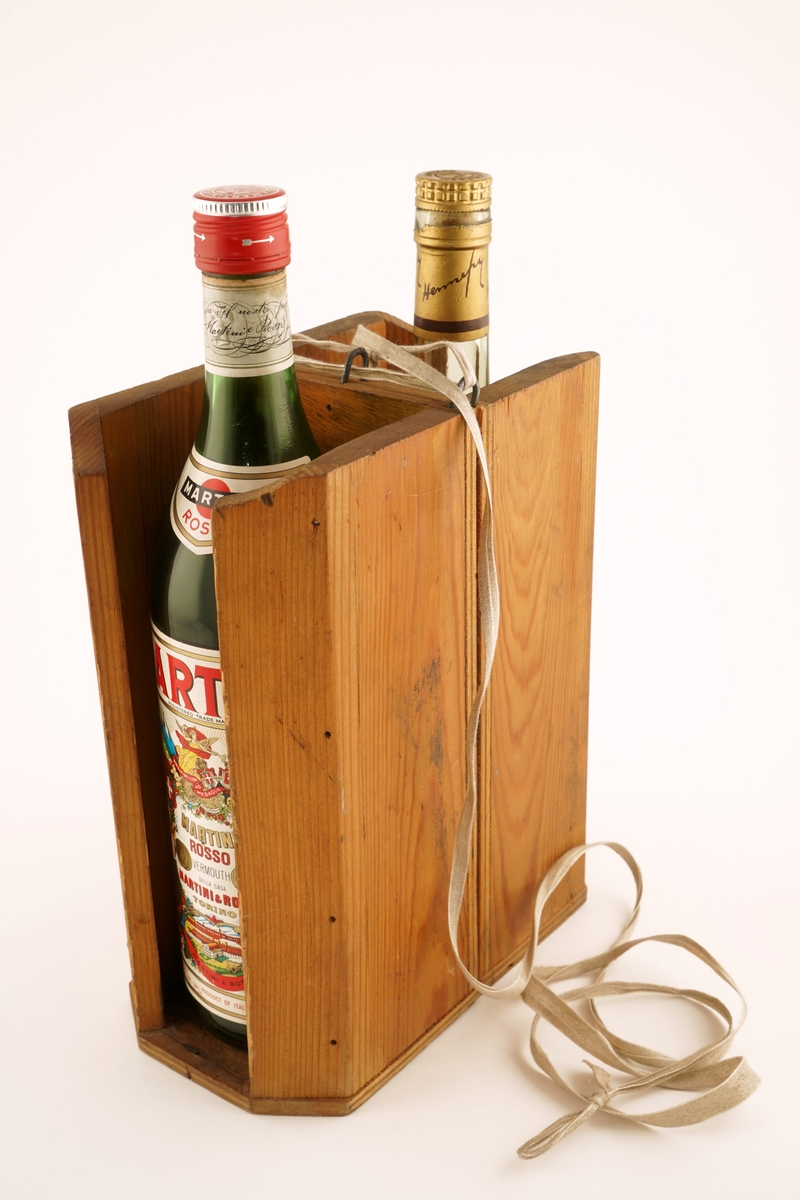 Hjemmelaget kasse for smugling av brennevin. Oljet treverk. Rektangulør med skrå hjørner og delvis
åpne kortsider. Det er plassert 2 flasker i kassen for å illustrere bruken. Ikke de opprinnelige.