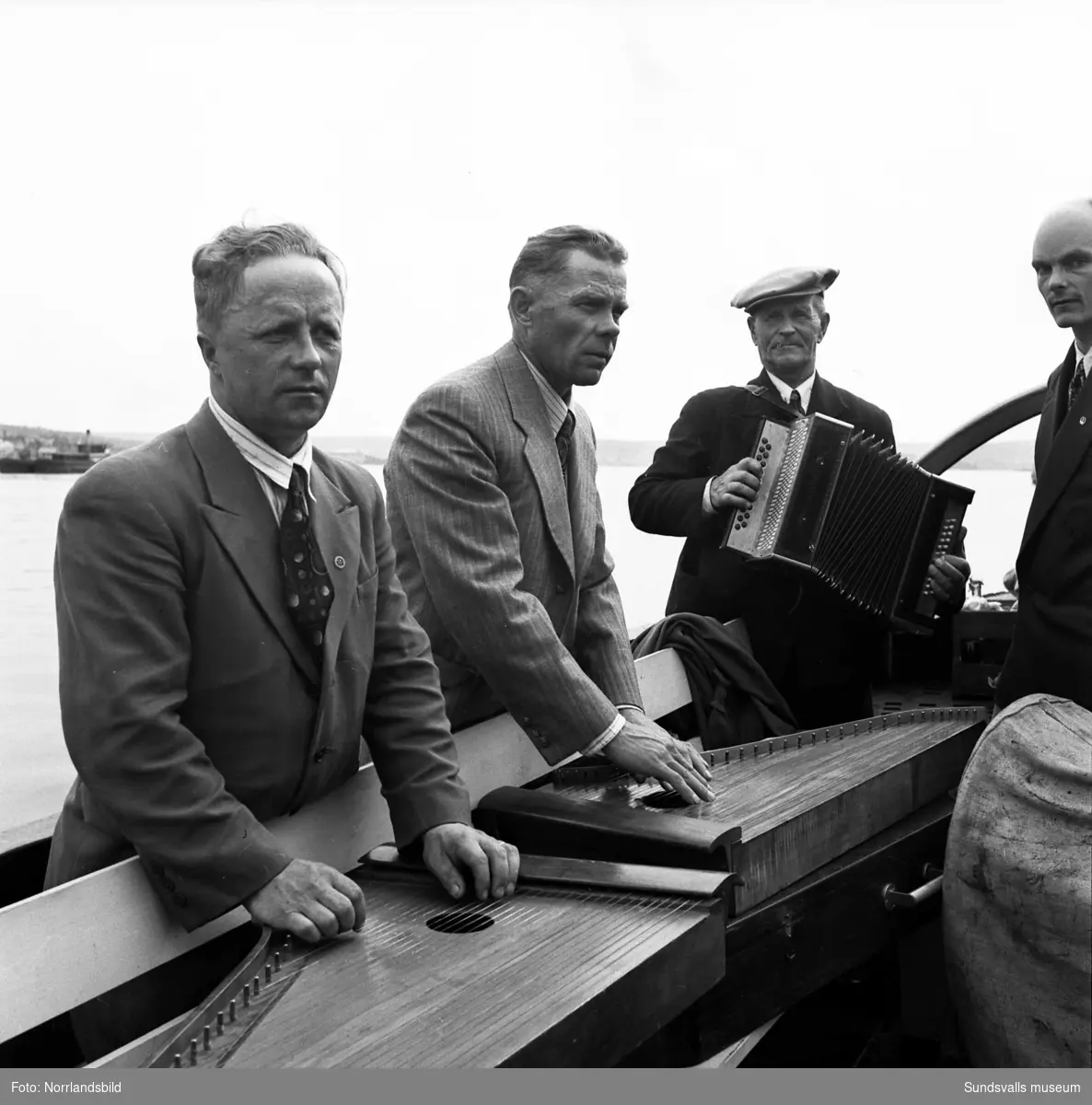 En grupp musikanter med sina instrument ombord på en båt i hamnen. Bilden tagen mot norra kajen och Heffnersområdet.