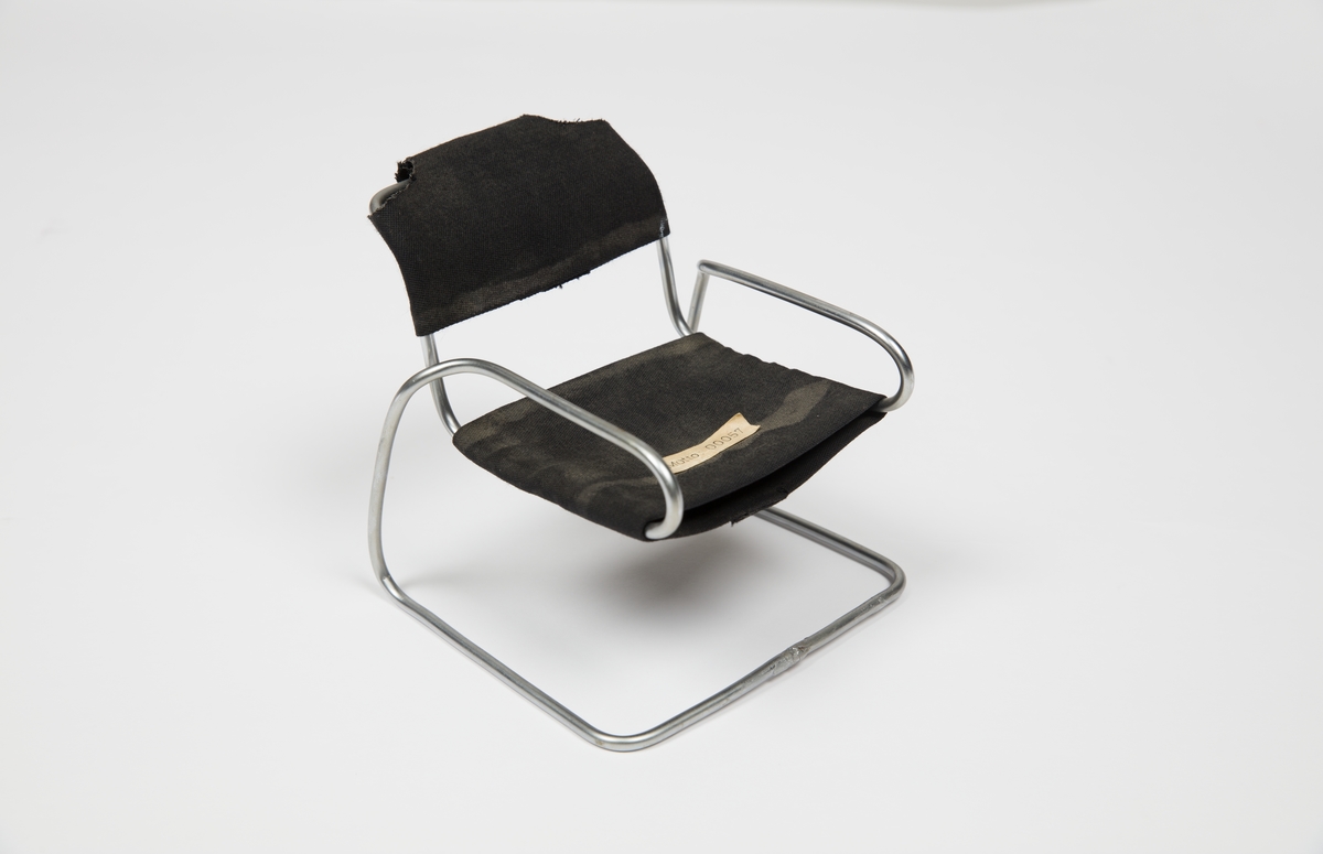 Skalamodell av en cantilever stol med metallstenger og svart stoff.