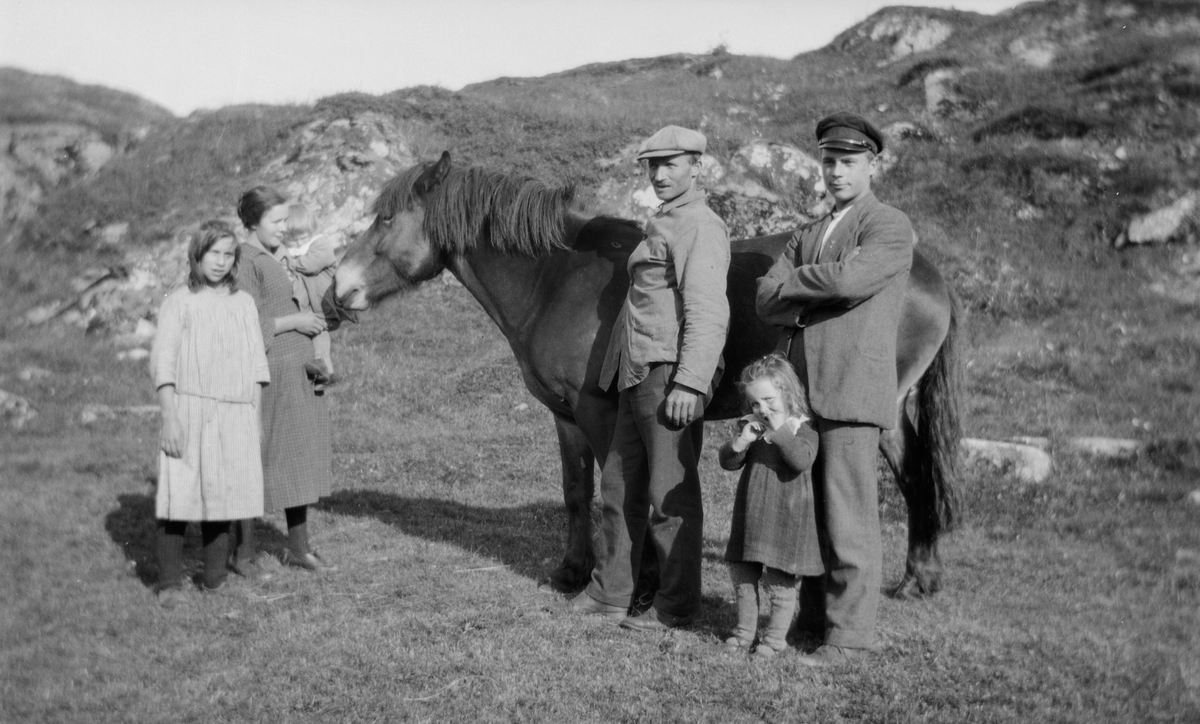 En kvinne, to menn og tre jenter med en hest.