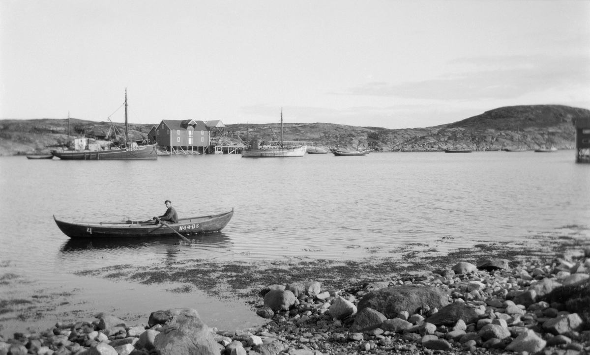 Mann i båt merket N-14-DS.  Brygge og flere båter i bakgrunnen.
Robåten med N-14-DS tilhører nok Må "Ågot" , for i merkeregisteret for 1920 skal "Ågot" være 33 fot :) og er kanskje en av gavlbåtene på andre sida. Må "Ågot er eid av Kr. Jørgensen ,Nordøyvågen.
Den svarte båten som har N-15-DS er Mk"Norddønna" , bygd 1896 , 59,1 fot , 44 Hk Avance. eid av partsrederiet Kr. Jørgensen , Nordøyvågen.