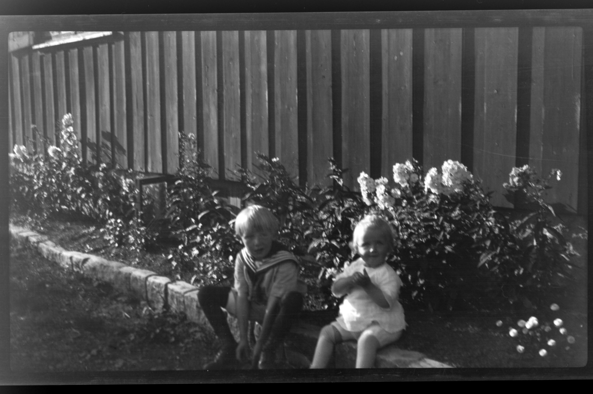Brødrene Rolf jr. og Julius Sundt sitter sammen ved et blomsterbed, Villa Knyggen, Voksenlia. Fotografert 1922.
