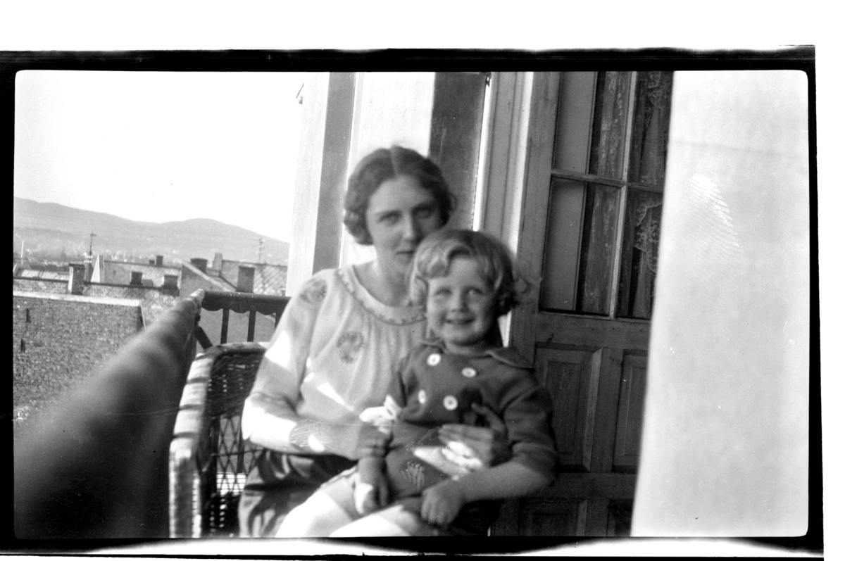 Hilda Sundt og sønnen Rolf Jr. på balkong i Thomas Heftyes gate 42E i Oslo. Utsikt over Oslos tak. Fotografert 1925.