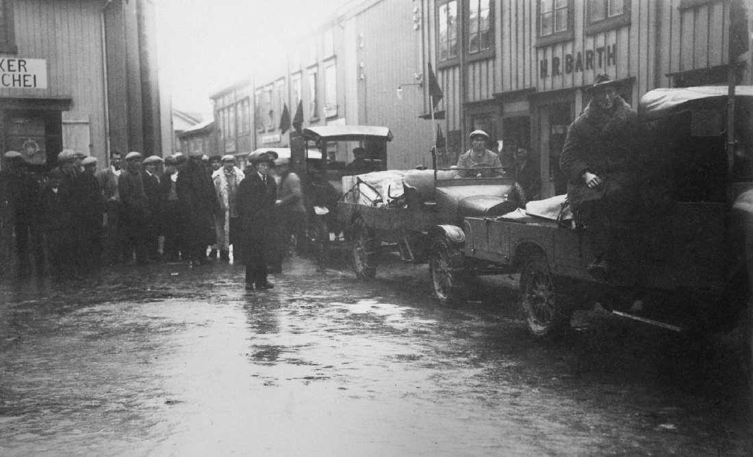 Sjogata. Transport av sprengstoff?. Biler med "røde?" flagg, mye folk. Til høyre H.R. Barth, til venstre skimtes Urmaker Schei.