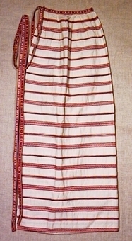 Förkläde med veckad överkant av tyg med röda ränder på vit botten. Förklädets band avslutas med fransar.
