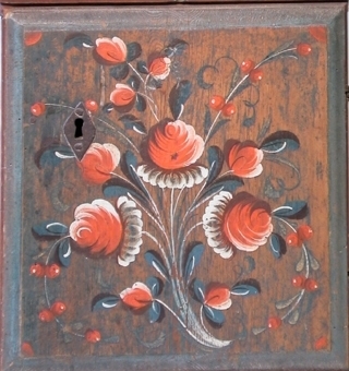 Hängskåp av trä med enkellucka och rakt överskjutande krön, målat i brunrött. På lucka och krön blomsterornering i rött, blått, vitt och mörkviolett.