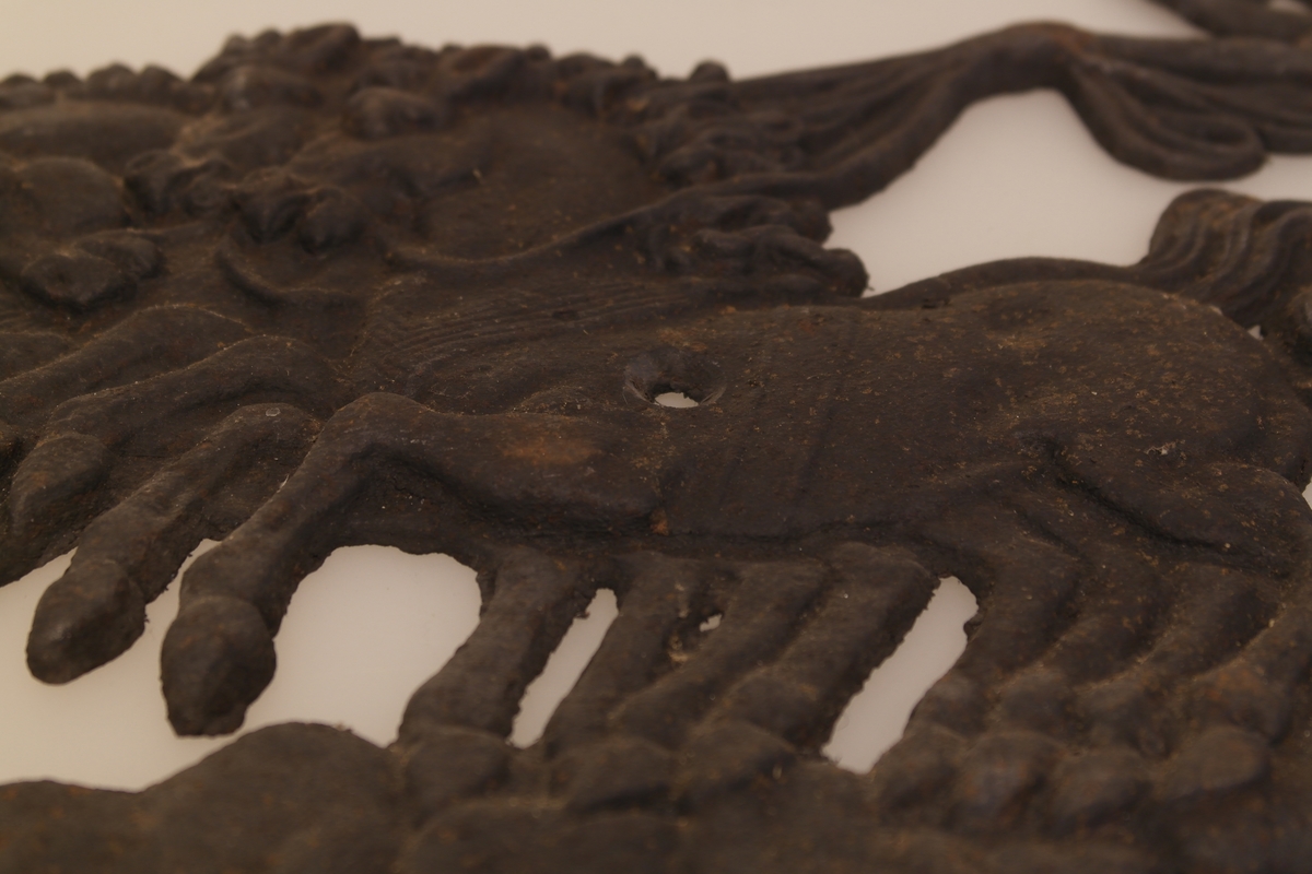 Ovnsrelieff i støpt jern. Relieffet forestiller en gudinne i en romersk stridsvogn trukket av et firspann. To utsparinger (i en av hestene og i vognen), antakelig for skrue.