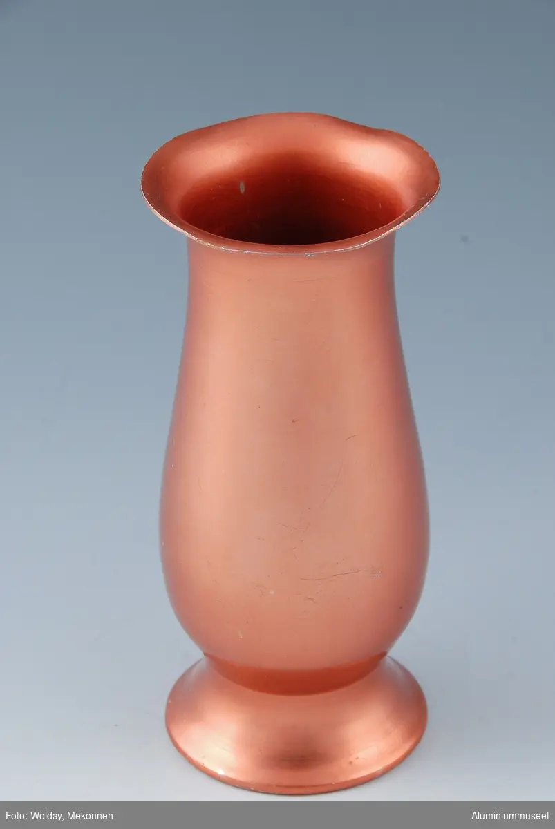 Teknikk: Vasen er trykket i trykkbenk på frihånd på sylindrisk dor. Det var spesielt Birger Hansen ( Se bilde nr.30 ) som mestret denne kunsten. Vasen ble polert eloksert og rødfarvet. 
Form: Sylindrisk vase med buet form
