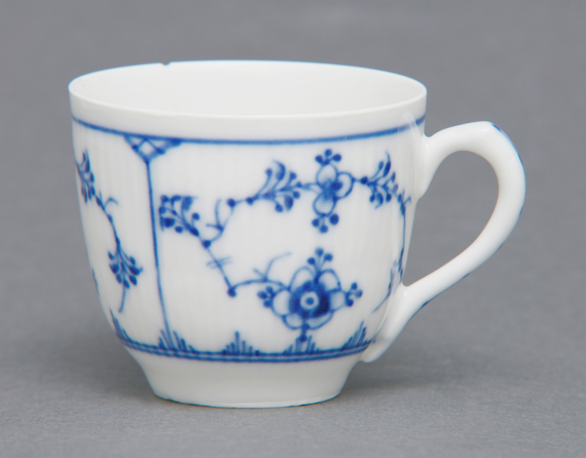 Sirkulær kaffekopp i porselen med glasur og hank. Rifler i porselenet og dekorert med stråmønster i blått. Tilhørende tefat (se relaterte objekter).
