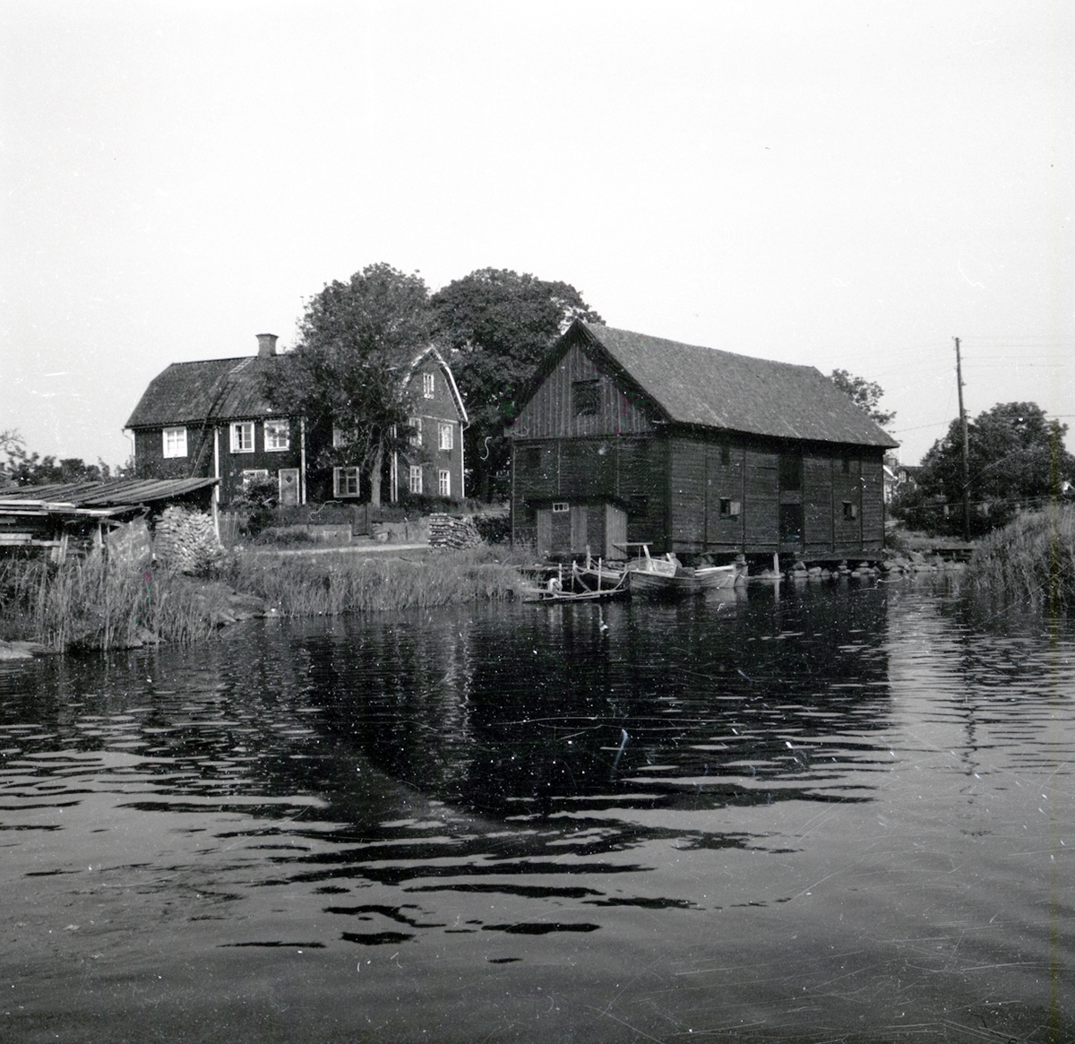 Kastmanska gården i Figeholm. I bilden syns ett bostadshus, en ekonomibyggnad, en brygga och två båtar.
