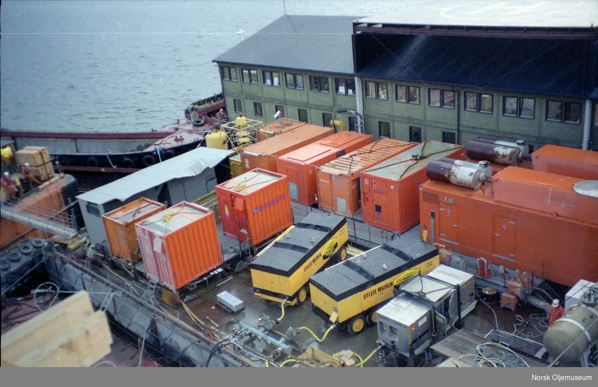 Draugen er under bygging i Yrkjefjorden i Vats, og diverse utstyr som kompressorer er plassert på en lekter for bruk under byggingen.