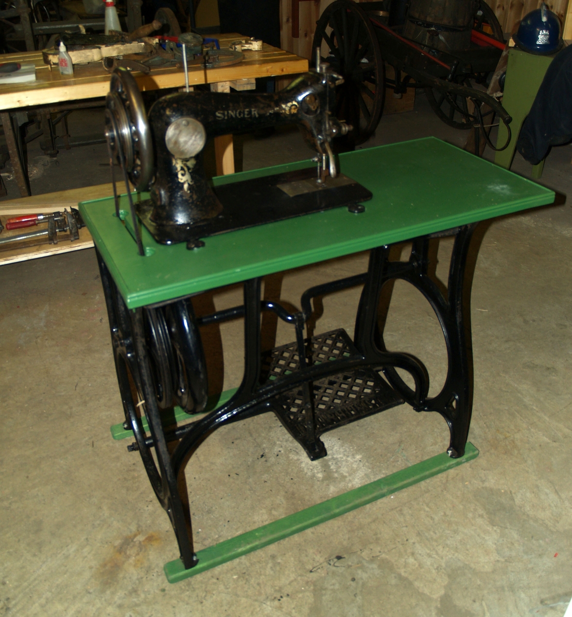 Symaskin med pedaldrift og montert i bord. Reimdrift fra hjul på understell til symaskinen. I Brannvesenet ble den bruk til sadelmakerarbeid og annet sømarbeid.