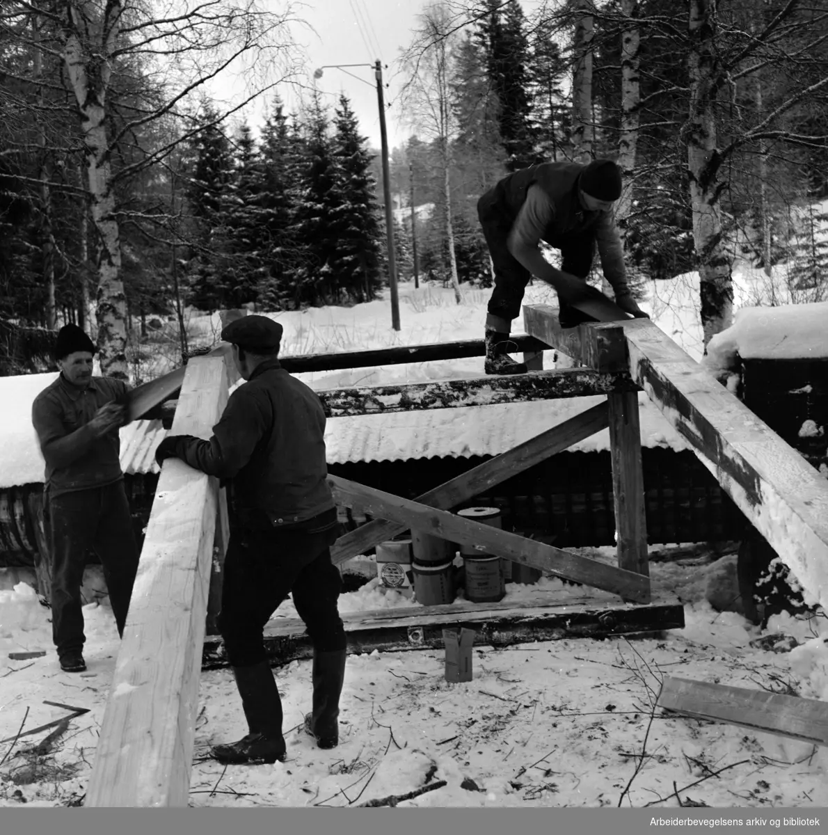 Østmarka: Løypa går ved Rustadsaga over Nøklevannsledningen, som tre menn nå slår en 16 meter bru over. Januar 1959