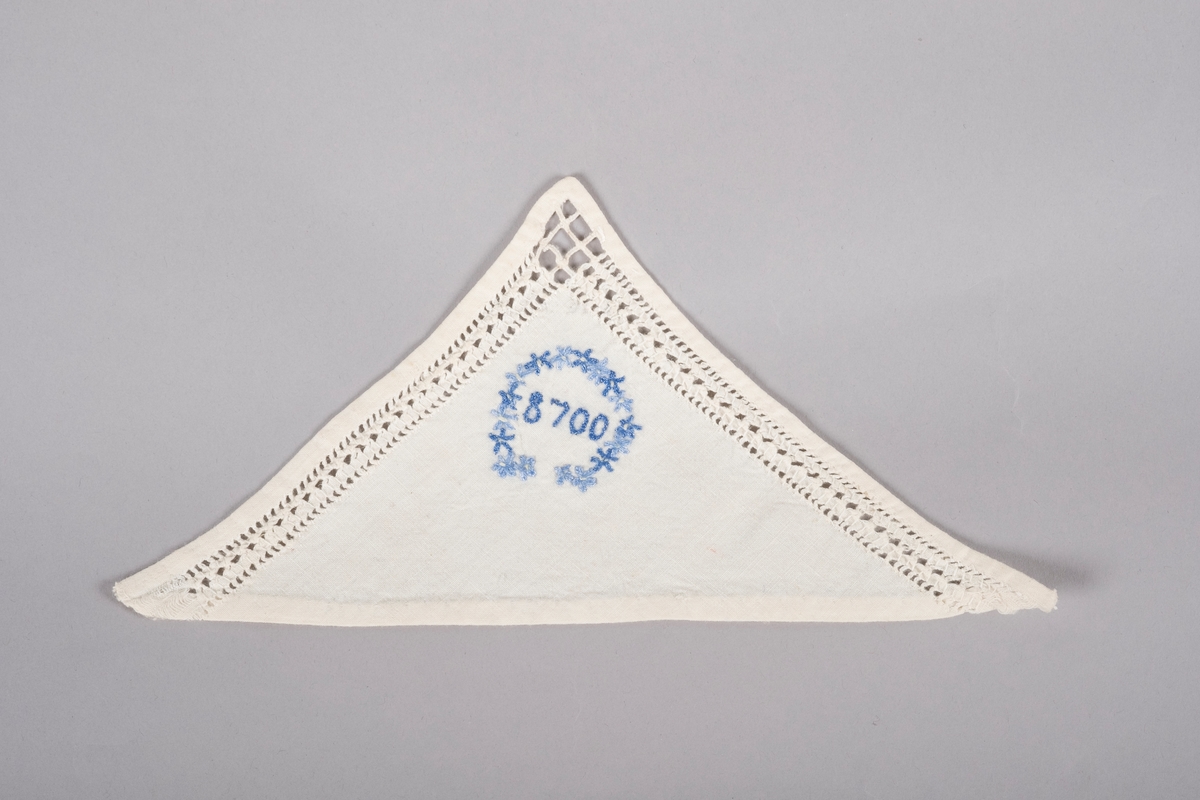 Hvit trekant lommetørkle med hullbroderier langs kanten og en brodert blå blomsterkrans rundt "8700", fangenummeret til Grete Wold.