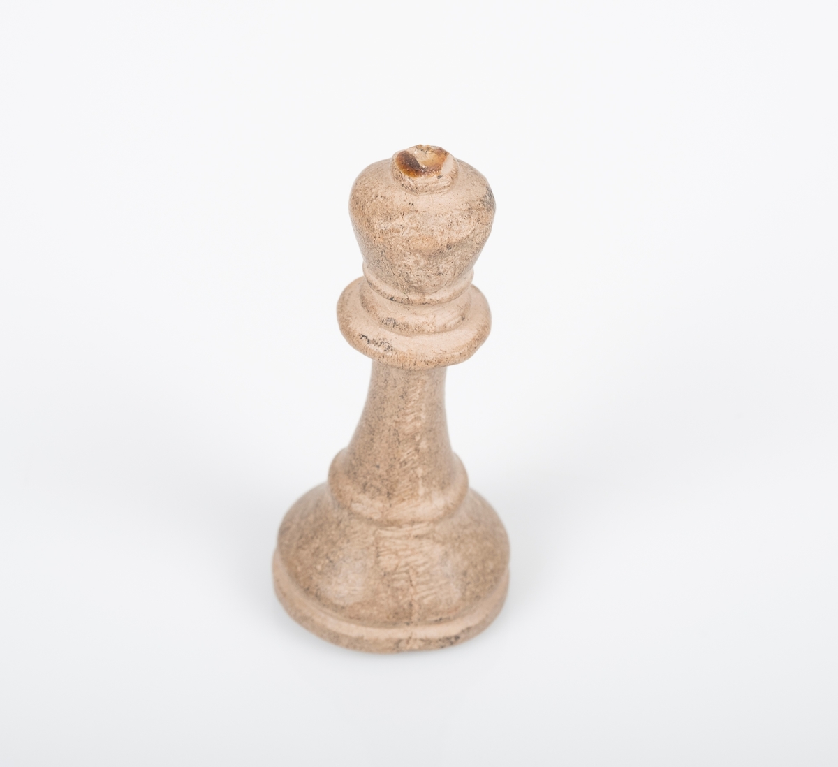 Sjakkbrikken (dronning) er laget av tre, og er malt hvit/grå. Det ser ut som den har blitt grå ved bruk. Lim på toppen av krona som tyder på at det har vært festet noe der, trolig et kors. Et lite hull på undersiden som er fylt med noe rosa.