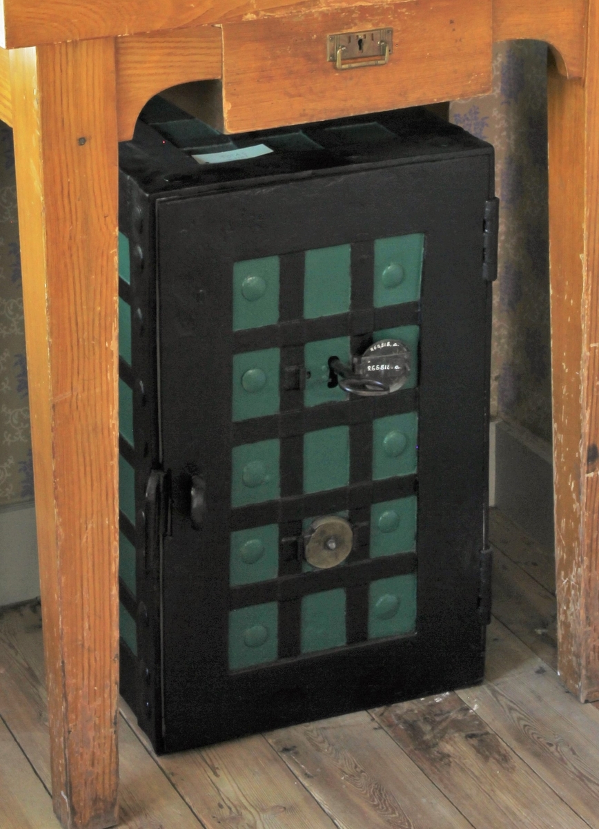 Kassaskåp av järn målat utvändigt i grönt och svart, stående rektangulärt. Dörr. Invändigt hyllplan och målat i ljusgult. Nyckel.
