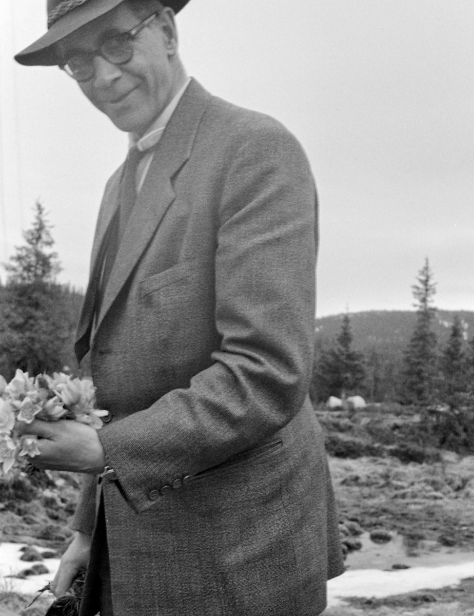 Direktøren i Glomma fellesfløtingsforening, ingeniøren Kaare Sparby (1904-2001). fotografert under ei befaring i Gausdal våren 1957.  Sparby var kledd i dress og hadde en vidbremmet filthatt på hodet.  I den ene handa holdt han en neve med blomster, antakelig mogop (Pulsatilla vernalis).  Sparby var sønn av Anna (f. 1875) og Arne Sparby (f. 1861) i Solør, som i Kaares oppvekstår var fløtingsfullmektig i Solør.  Med kompetanse fra ingeniørutdanning overtok sønnen seinere denne stillingen.  Derfra avanserte han, først til overinspektør og i 1950 til direktør i Glomma fellesfløtingsforening.  Denne posisjonen hadde Kaare Sparby til han ble pensjonist i 1973.
