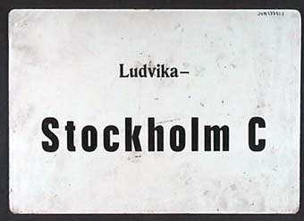 Dubbelsidig rektangulär plastskylt med svart text på vit botten:
"Ludvika-
Stockholm C"

Text på andra sidan:
"Stockholm C-
Ludvika"