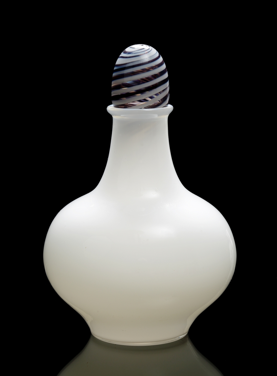 Urna "VIVA" i vitt opakt glas. Propp med spunnen glastråd i vitt och svart.
Urnan kalebassformad.