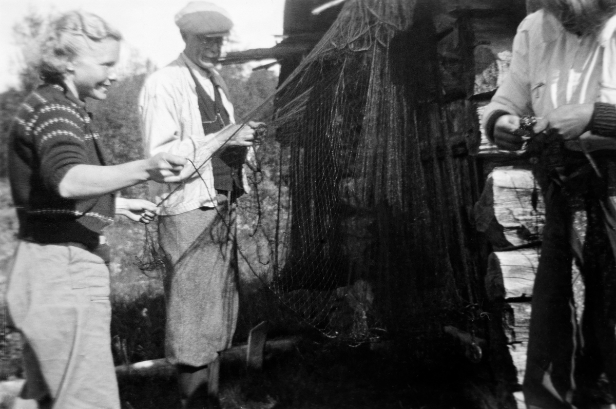 Ordning av fiskegarn ved en husvegg i Spekedalen i Tynset kommune i Nord-Østerdalen.  Den unge kvinna til venstre var lokal og hadde etternavnet Skancke.  Den noe eldre mannen ved siden av er tannlege Ragnar Horst, som ellers bodde i Elverum.  Bildet skal være tatt i 1942.