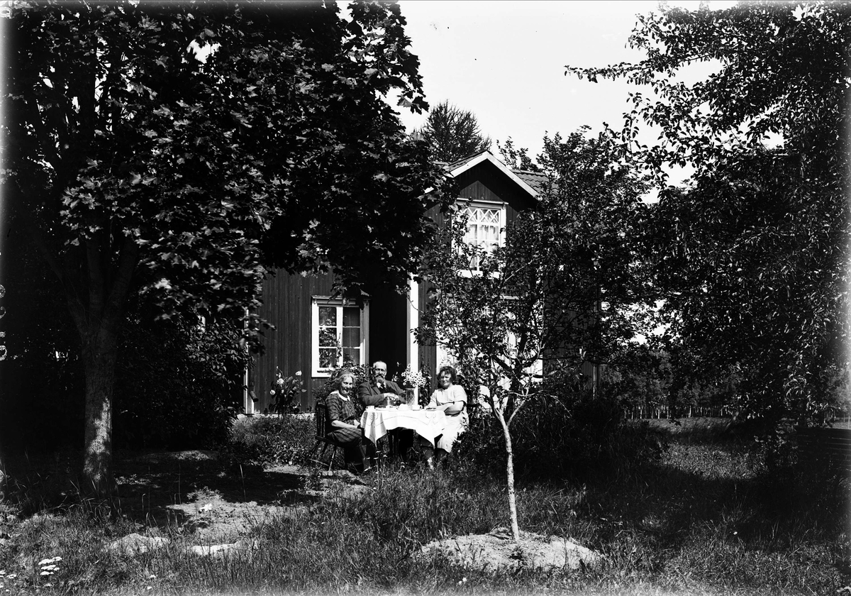 Mattis Andersson och paret Forsell vid kaffebord framför hennes stuga, Berga mossen, Simtuna socken, Uppland 1926