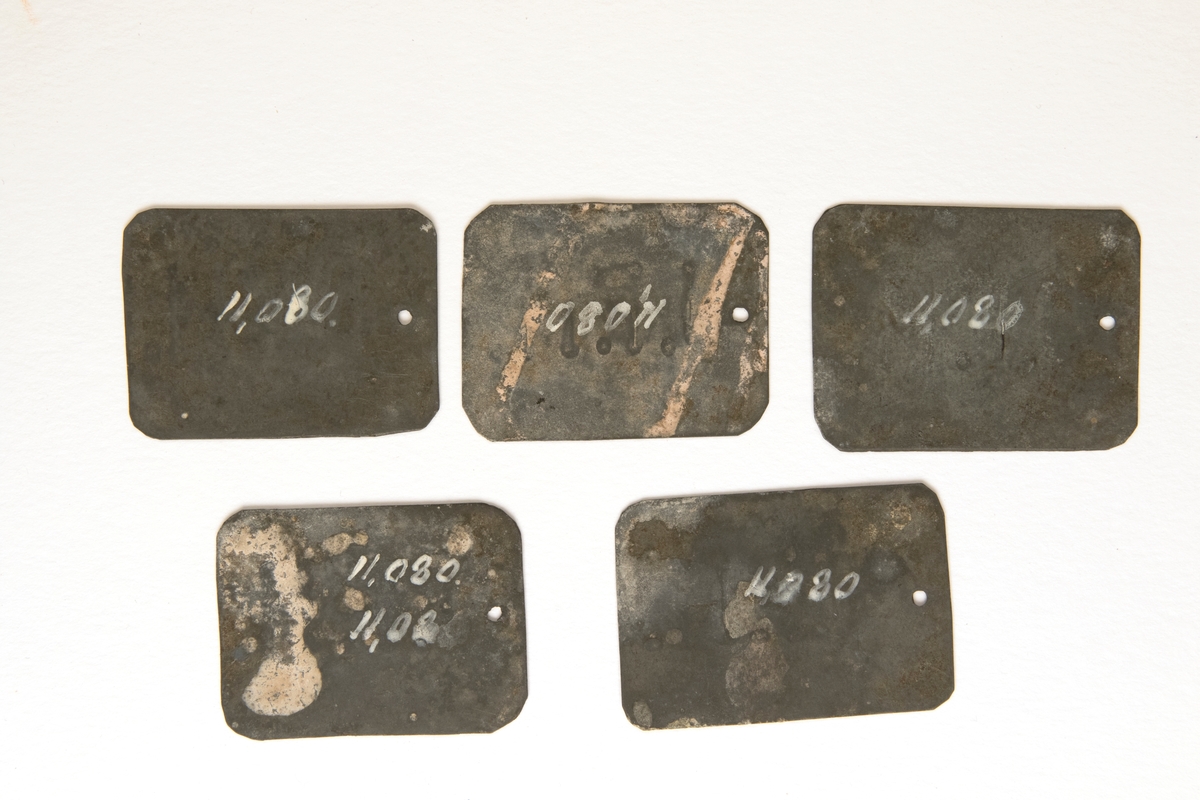 Plåtbrickor, 5 st, rektrangulära, präglade med bokstäverna "J.F.H" på ena sidan. Ett litet hål finns i kortänden för fastsättning.