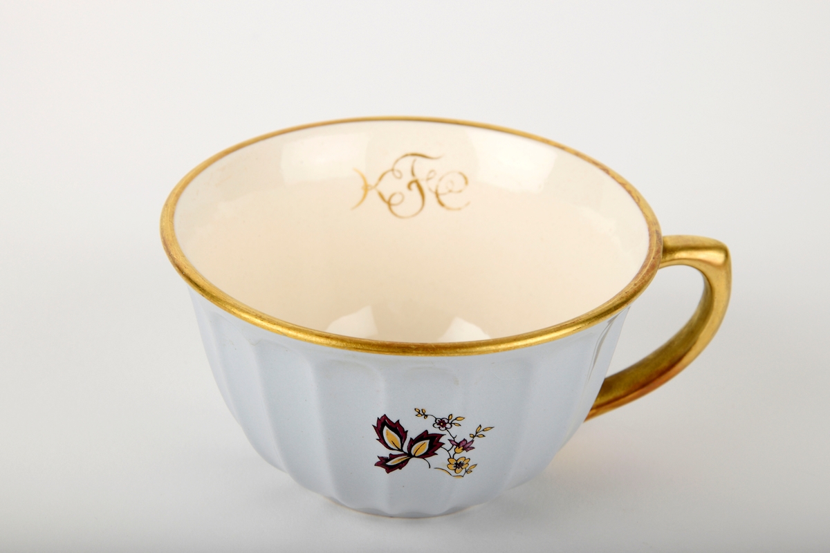 Lilla og gull blomstermotiv på hver side av koppen.