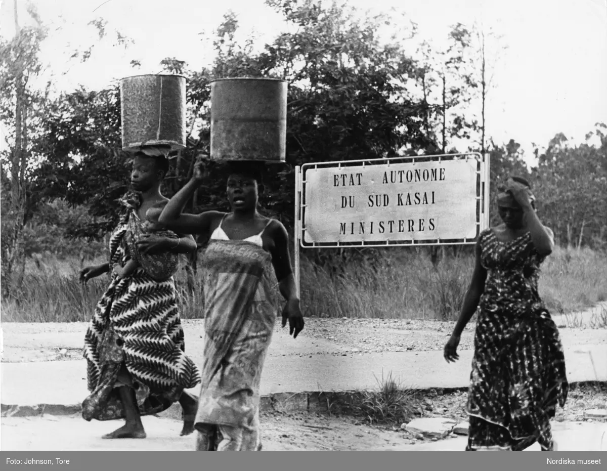 Kongo. "Balubakvinnor bär vattenkärl framför entrén till ministerieområdet i Bakwanga, Syd-Kasai".