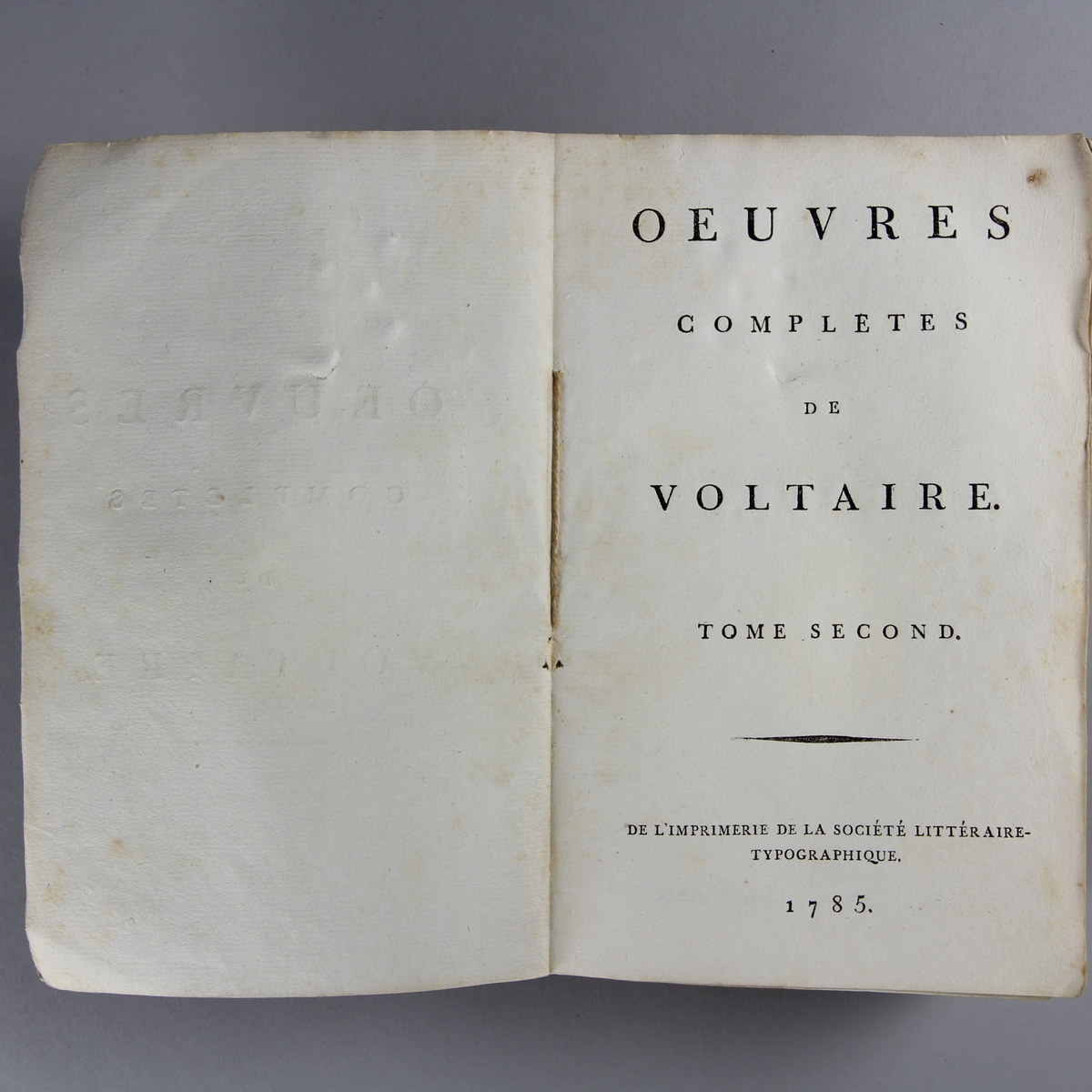 Bok, häftad, "Oeuvres complètes de Voltaire." del 2, tryckt 1785.
Pärm av gråblått papper, skurna snitt. På ryggen pappersetikett med tryckt text med volymens namn och nummer. Ryggen blekt.