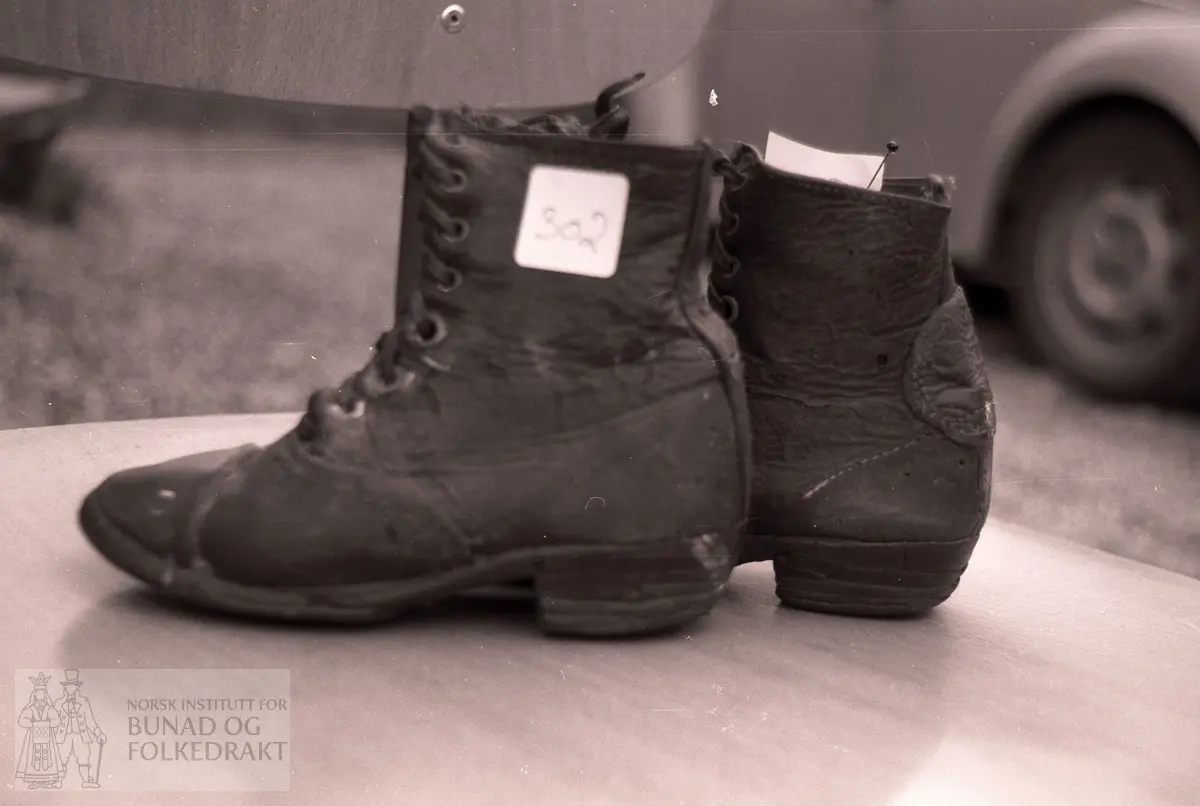 Lærsko, brune snøresko med 8 hull på hver side, den ene skoen er lappet bak.  Trolig brukt først på 1900.