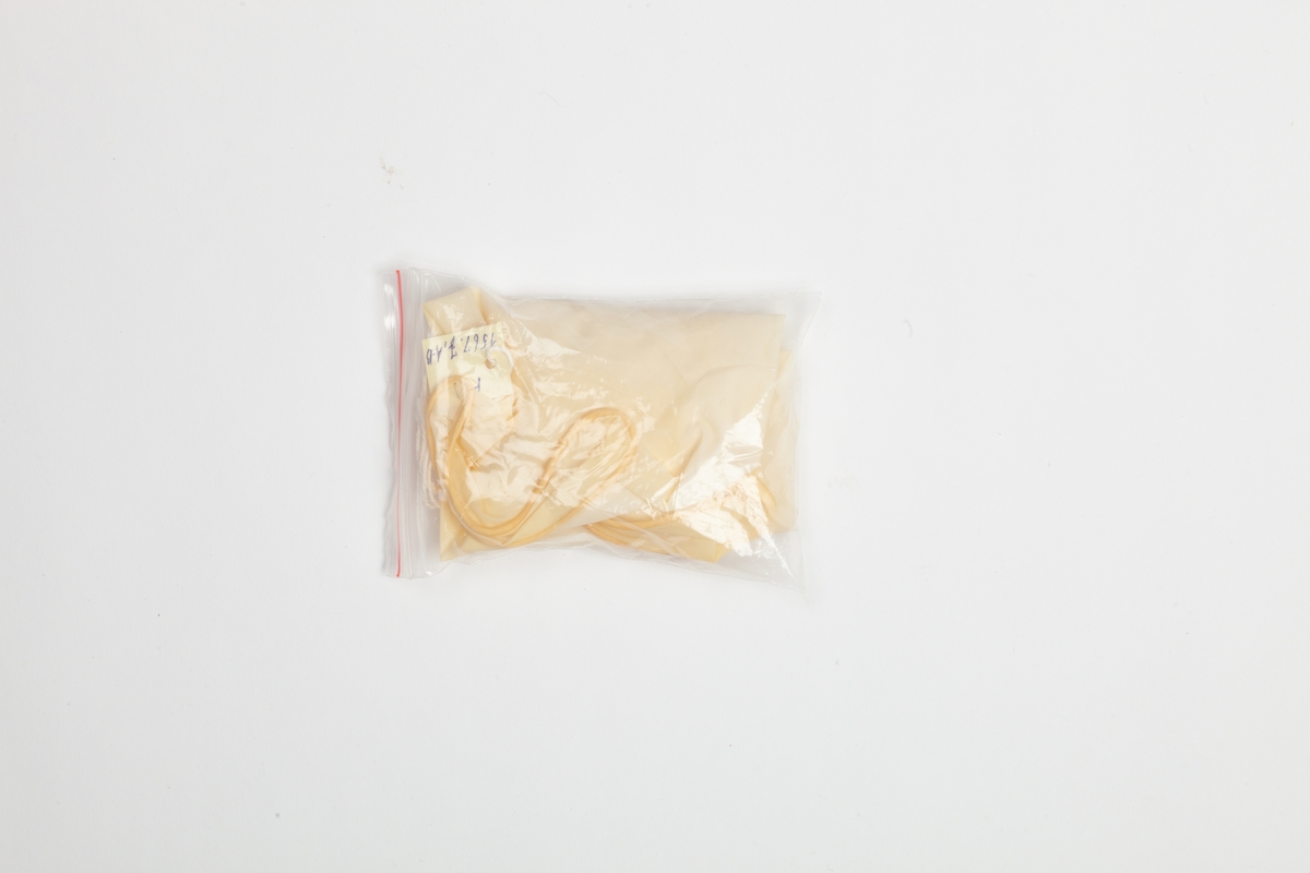 Et par latex (2. stk.) hansker i en liten plastpose med lukning. Hanskene er engangshansker i gult mykt plastikk. Plastposen er gjennomsiktig og med lukning i den ene enden.