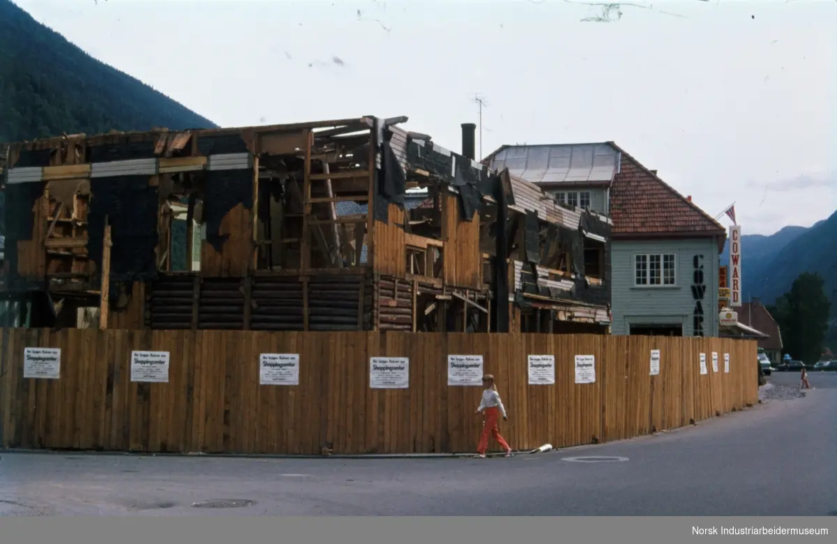 Delvis revet bygg bak anleggsgjerde med plakater hvor det står "Her bygges Rjukans nye shoppingsenter".