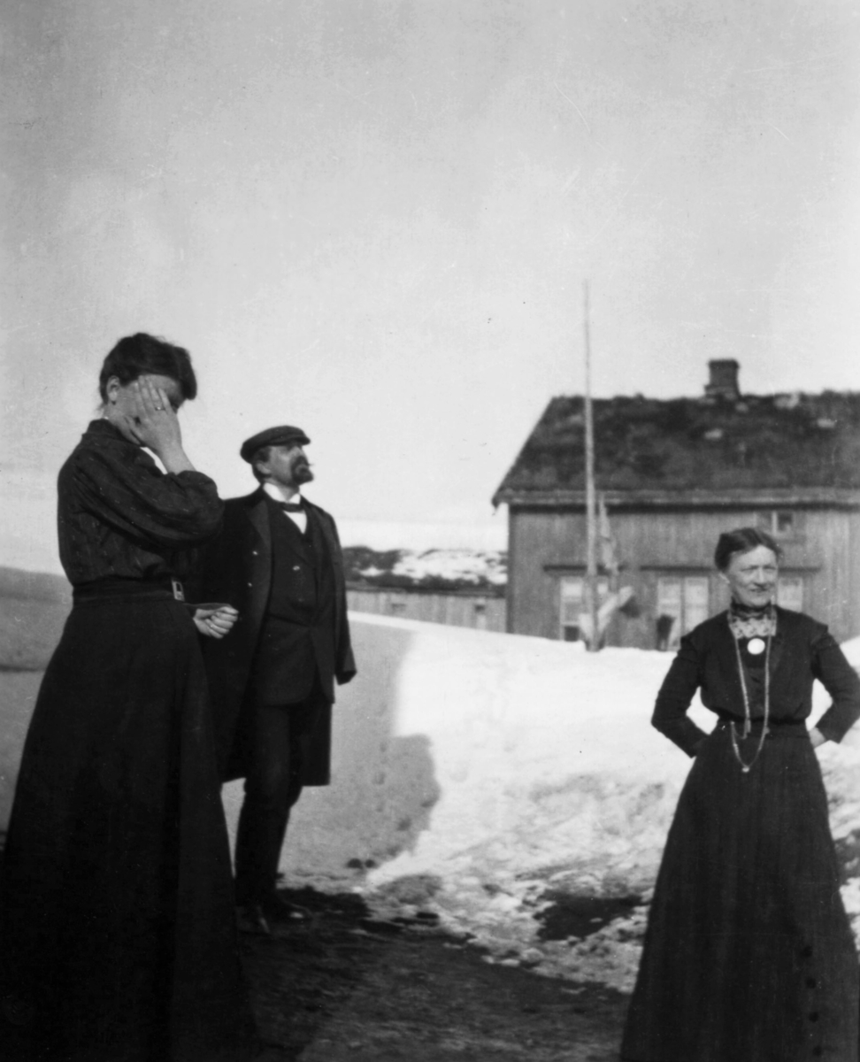 To kvinner og en mann står ved postkontoret i Båtsfjord 1910. Mannen på bildet er postekspeditør Rasmus Kyvik, kvinnen til høyre er postbud Iversen og damen til venstre er muligens telegrafisten.