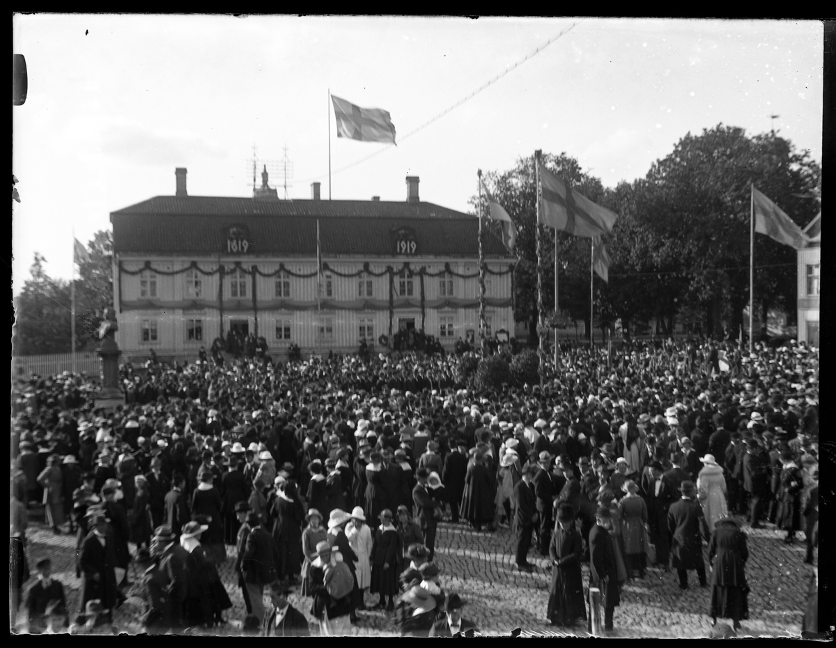 Folksamling på Stora torget för att fira Alingsås stads 300års jubileum. I bakgrunden syns Rådhuset dekorerat med lövgirlanger.