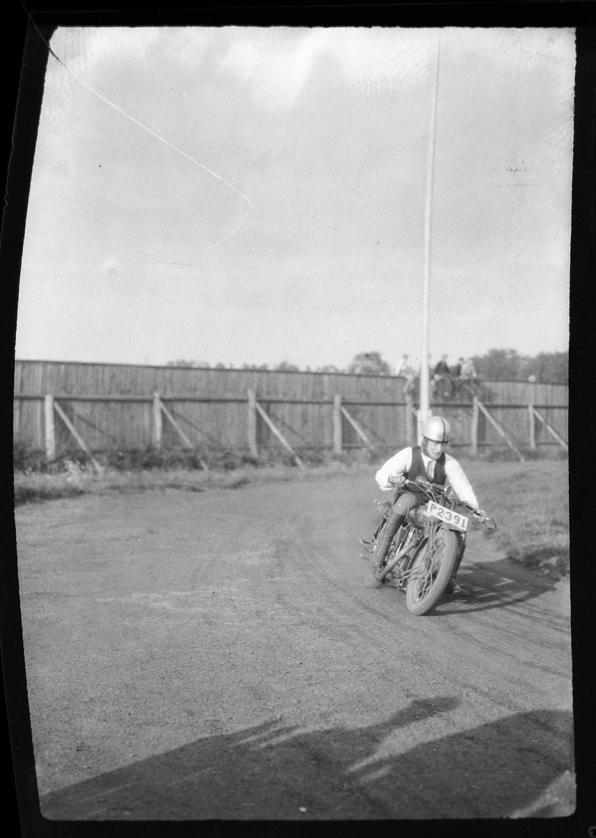 En man kör motorcykel på en grusad bana. I fotografens anteckningar står det: "2 film från Motorcykellopp (Idrottsp.)".