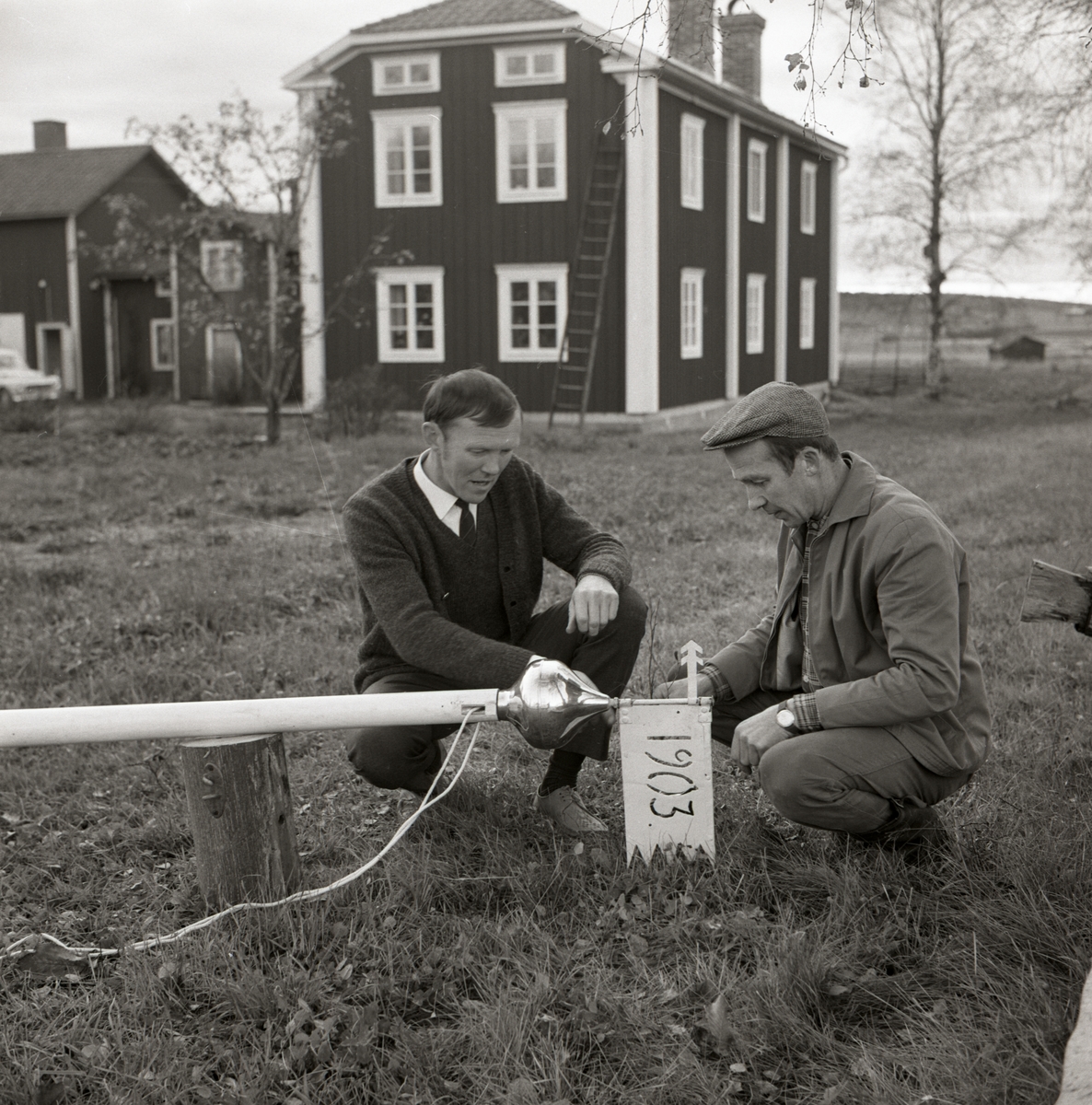 Två män sätter fast en vindflöjel i toppen på en flaggstång vid gården Sunnanåker, 1967-68.