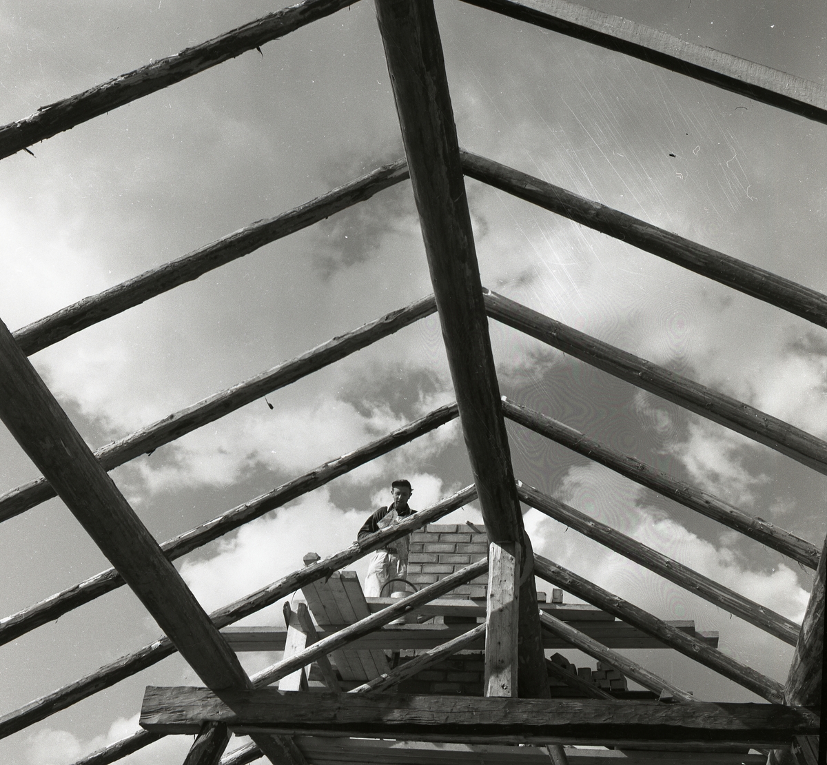 En man står på en byggställning och murar skorsten på ladugården, Sunnanåker 14 juni 1956.